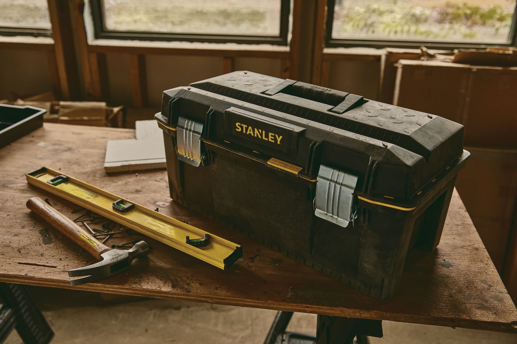 Stanley 023001W Werkzeugkasten mit Metallverschlüssen auf Werkbank, Hammer und Wasserwaage daneben.